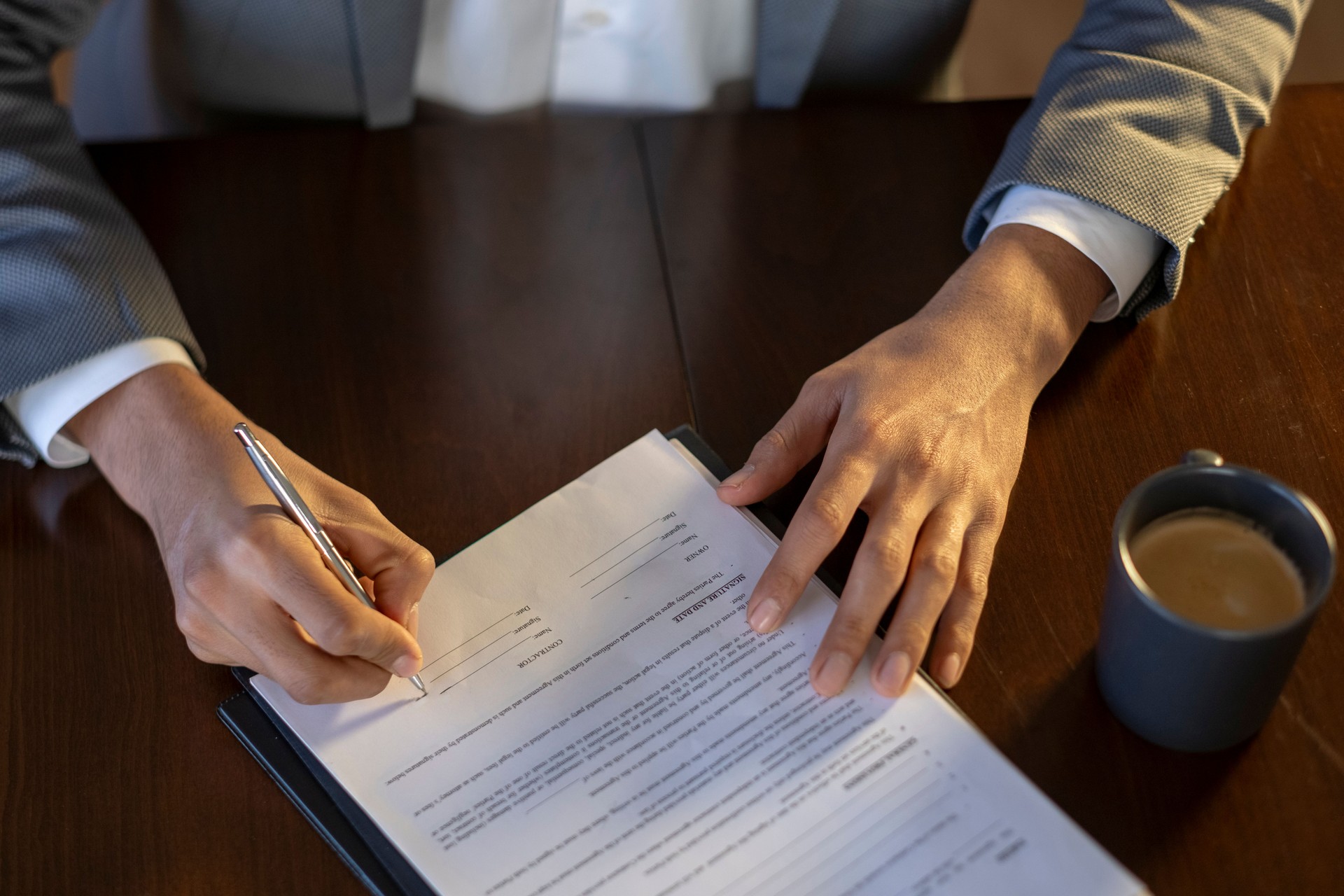 Businessman signing a contract at his desk with coffee